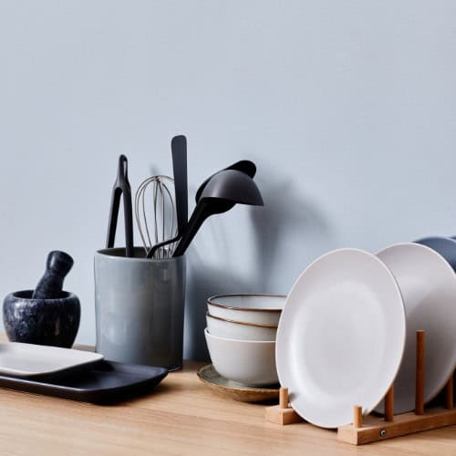 Plates, bowls, utensils, cutlery on kitchen work surface.
